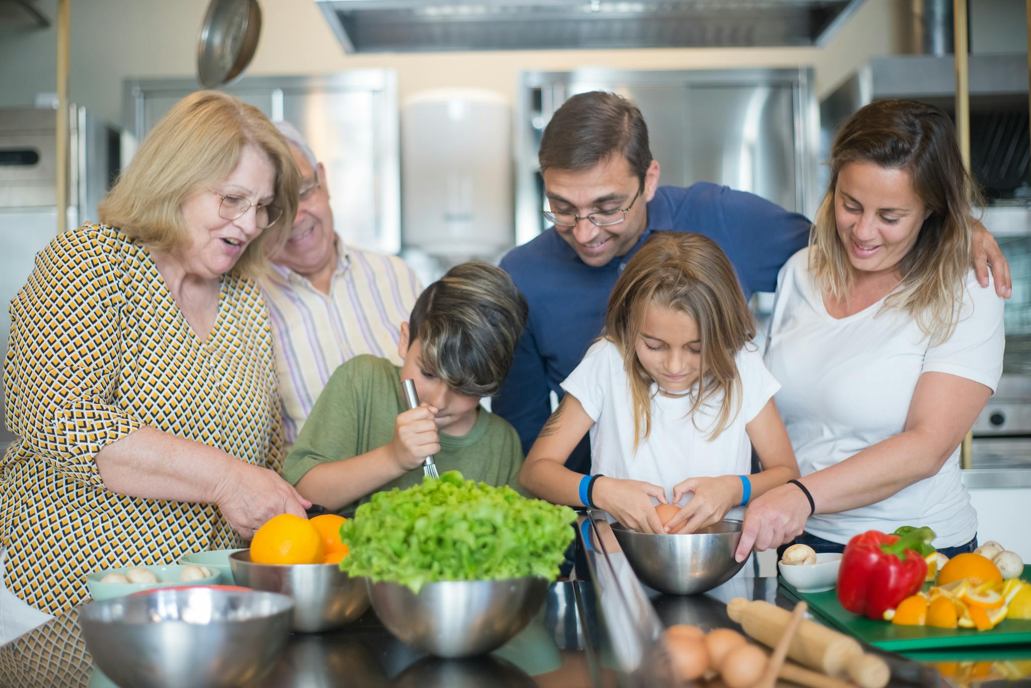 Family of various ages gathers in kitchen to cook meal together, showcasing culinary togetherness.